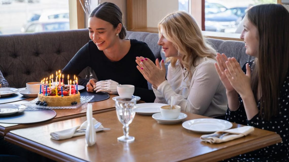 Friends celebrating a birthday with cake and laughter in a cozy café setting.