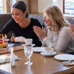 Friends celebrating a birthday with cake and laughter in a cozy café setting.